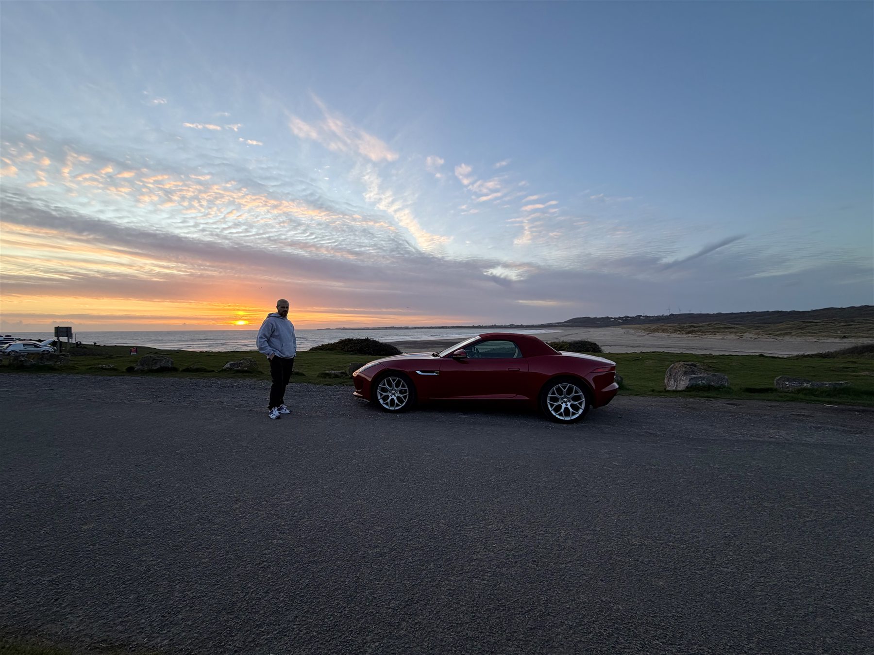 Josh Llewellyn-Jones beside a red Jaguar at sunset